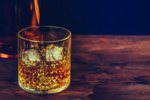 Glass Of Whiskey With Ice Cubes Near Bottle On Wood Table, Warm
